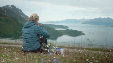 Nordic-Blonde-Girls-Sitting-in-the-Grass-and-Having-Picnic-in-a-Beautiful-Norwegian-Fjord,-Hiker-Girl-Eating-Lunch,-Kvænangsfjell-Gildetun,-Sørstraumen