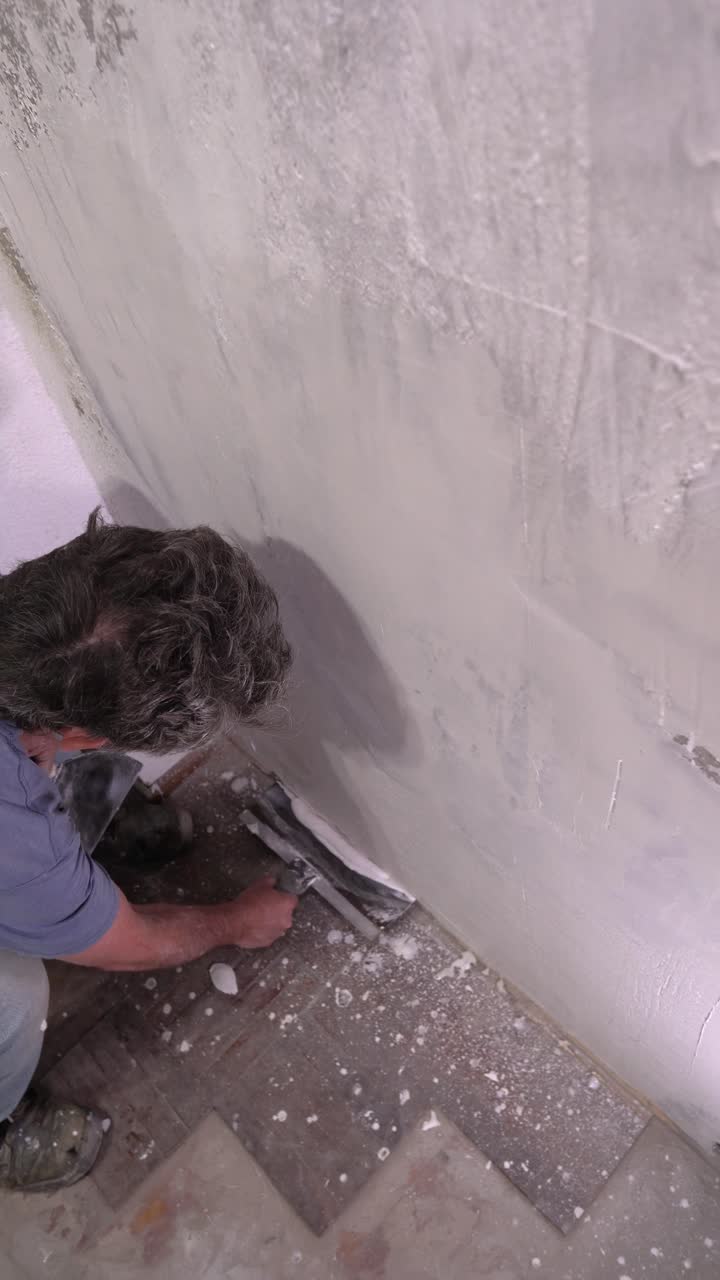 A professional worker uses a trowel to apply joint compound or plaster to a wall surface, performing the final finish in a room