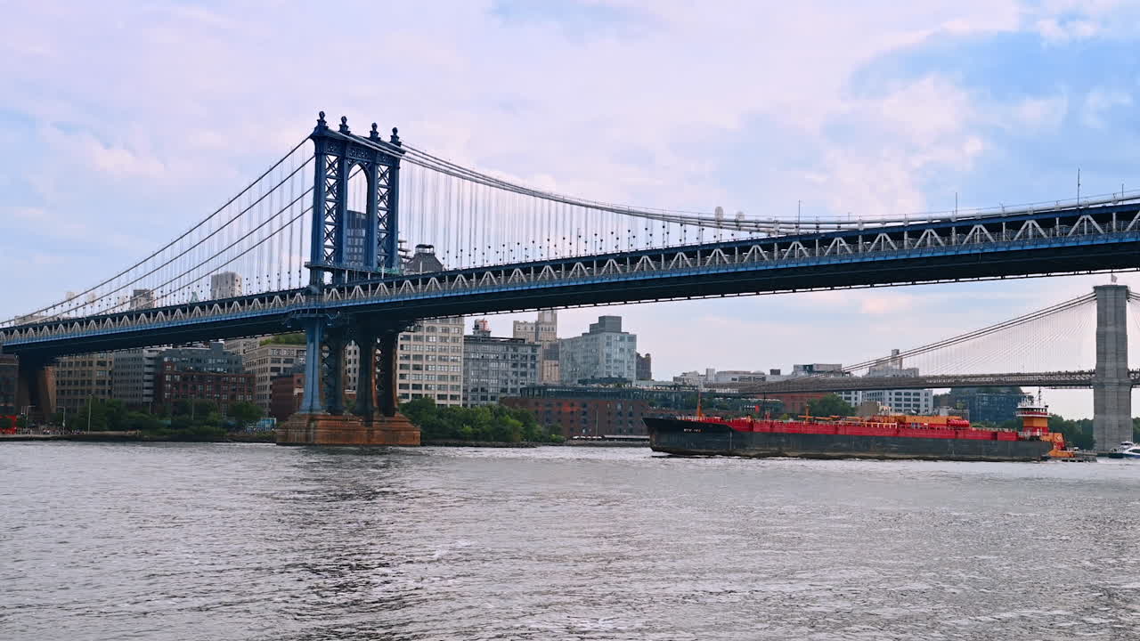 A barge moving slowly by the East River under the Manhattan Bridge. New York skyline at backdrop
