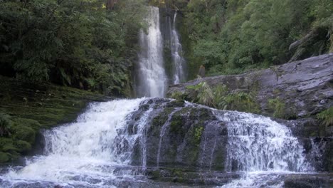 una turista moviéndose a lo largo de la superficie rocosa observando la hermosa vista de las aguas que fluyen a través de las rocas en nueva zelanda - plano medio