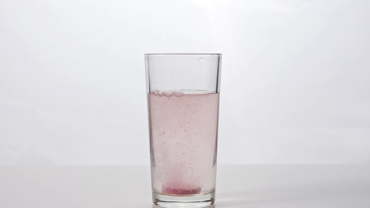 색 배경에 있는 물 한 잔에 부풀어오르는 태블릿이 떨어집니다.