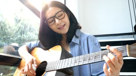 attractive asian woman playing guitar with smiling at home.