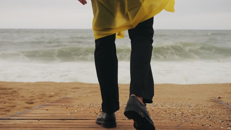 Man tourist person with umbrella and raincoat near sea ocean beach with storm on rainy european city street, lights reflecting, walking in Barcelona or Amsterdam during the rain
