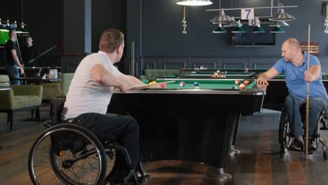 hombres adultos con discapacidad en silla de ruedas juegan al billar en el club