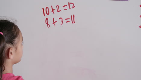 niña de escuela primaria haciendo matemáticas en la pizarra, vista trasera