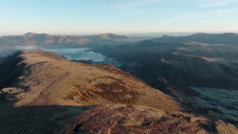 Mountains-to-the-horizon-with-shadowed-valley-and-lake-in-dawn-autumnal-sunshine-with-high-altitude-flight-over