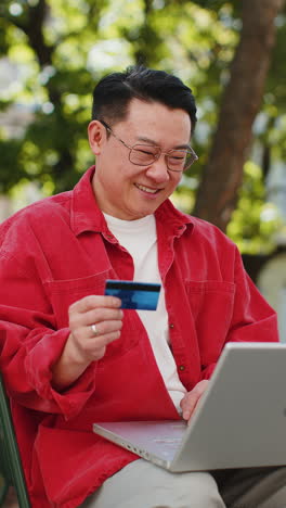 Asian-mature-man-using-credit-bank-card-and-laptop,-transferring-money-purchases-online-shopping