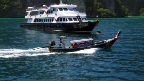 a fisher boat passing by a huge ferry while swiftly traversing the sparkling blue ocean on a sunny day in thailand- wide shot