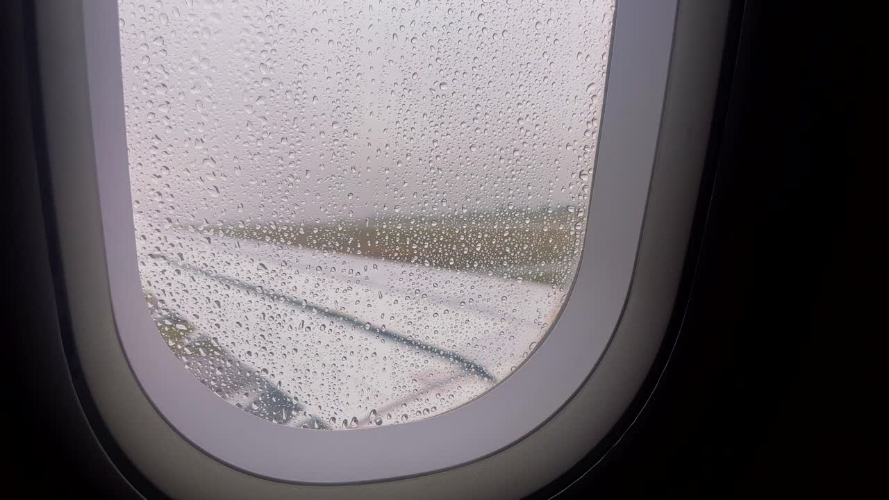 Raindrops on an airplane window with a blurred runway in the background
