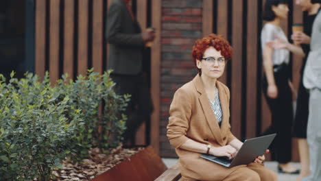 redhead businesswoman working on laptop on street