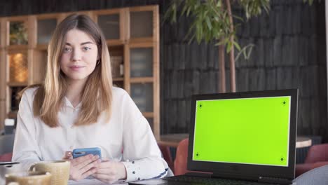 Attractive-young-woman-is-sitting-near-the-laptop-showing-a-green-screen