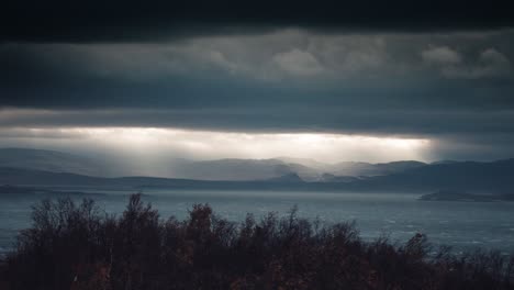 sonnenstrahlen durchdringen die dicke, bedrohliche wolkendecke über dem fjord und erhellen das wasser darunter