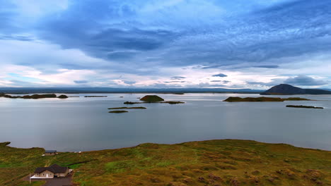 Rising over the rocky shore with some cottages on. Revealing view on the calm waterscape with some stones sticking out of water. Iceland nature.