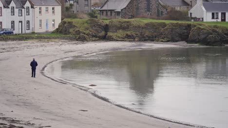 Person-Walking-Along-Clean-Beach-With-Dark-Water-Wide