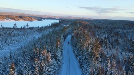 aerial of a car driving down a snowy road in the middle of winter