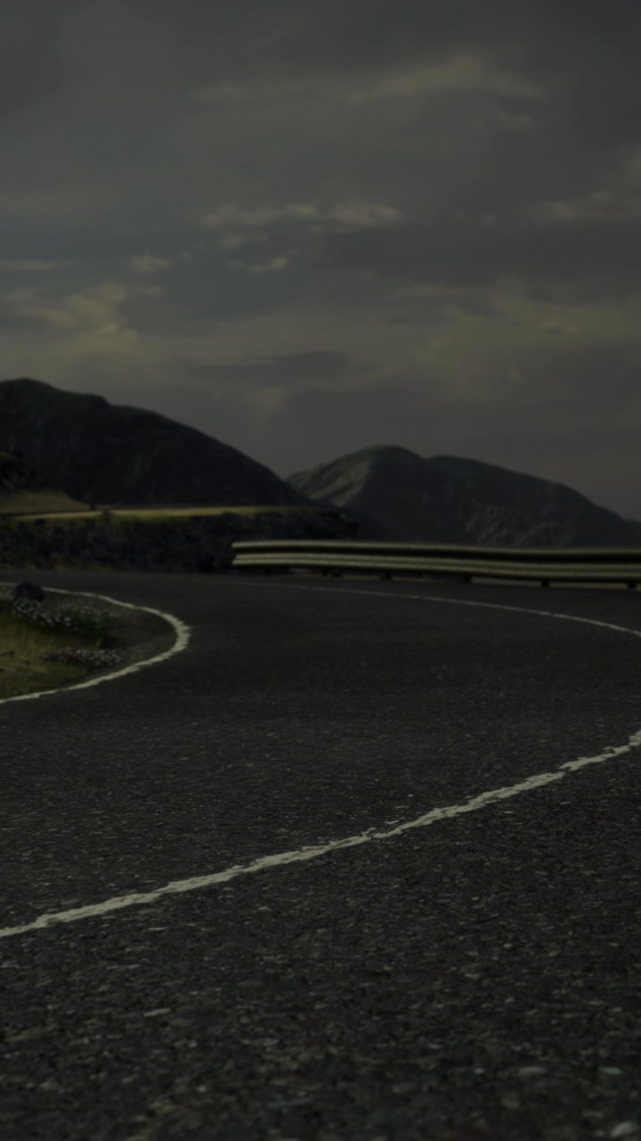 Curved road cuts through a mountainous area under a cloudy sky