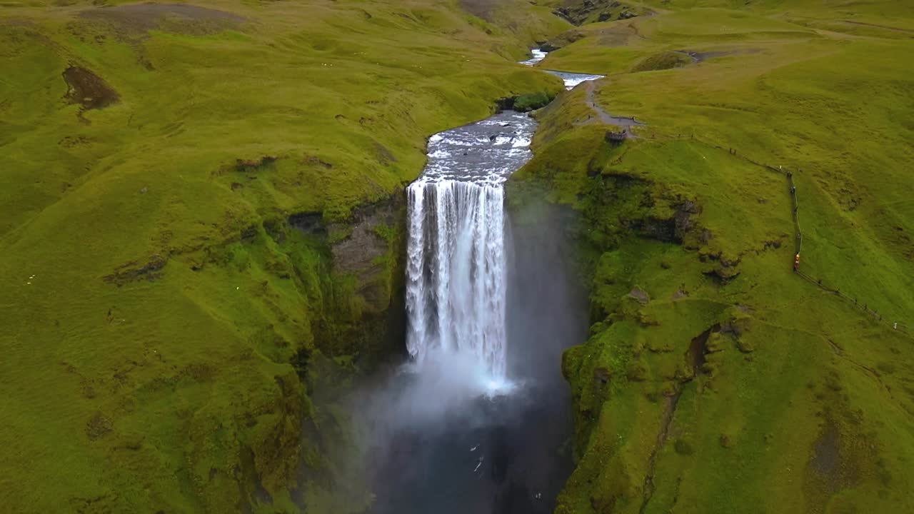 4K cinematic drone footage of Skógafoss Waterfall in Iceland, capturing the immense curtain of water cascading from towering cliffs surrounded by lush green landscapes. Iceland_25