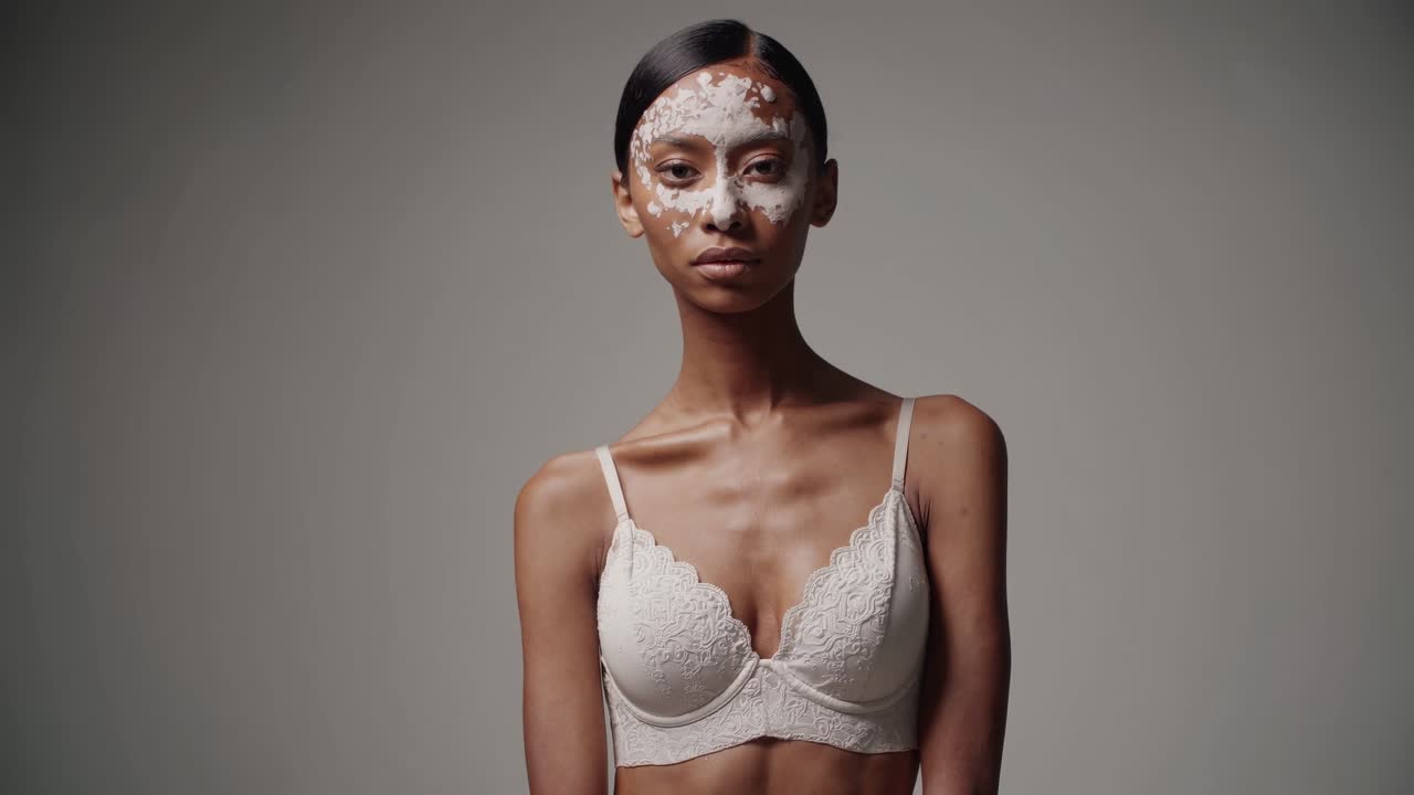 Studio portrait capturing a confident young woman with vitiligo, wearing a beauty mask and embracing skincare, highlighting themes of self acceptance and body positivity