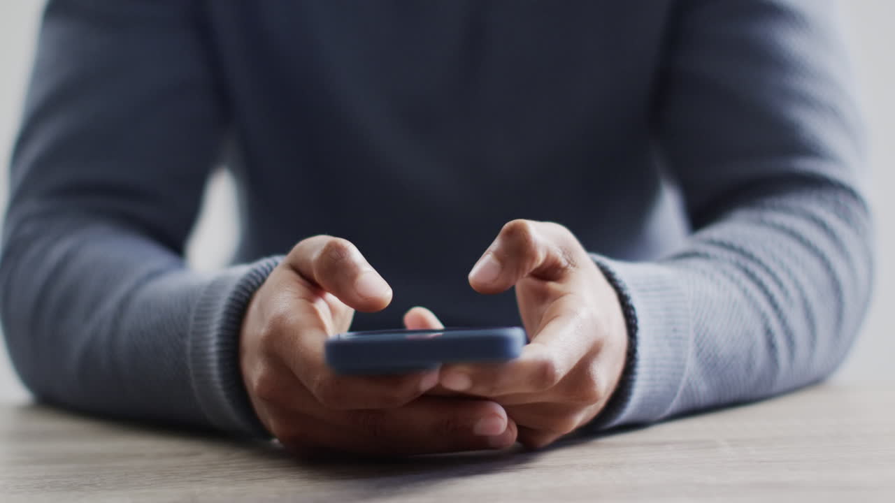 video de la sección media de un hombre de negocios biracial en el escritorio usando un teléfono inteligente