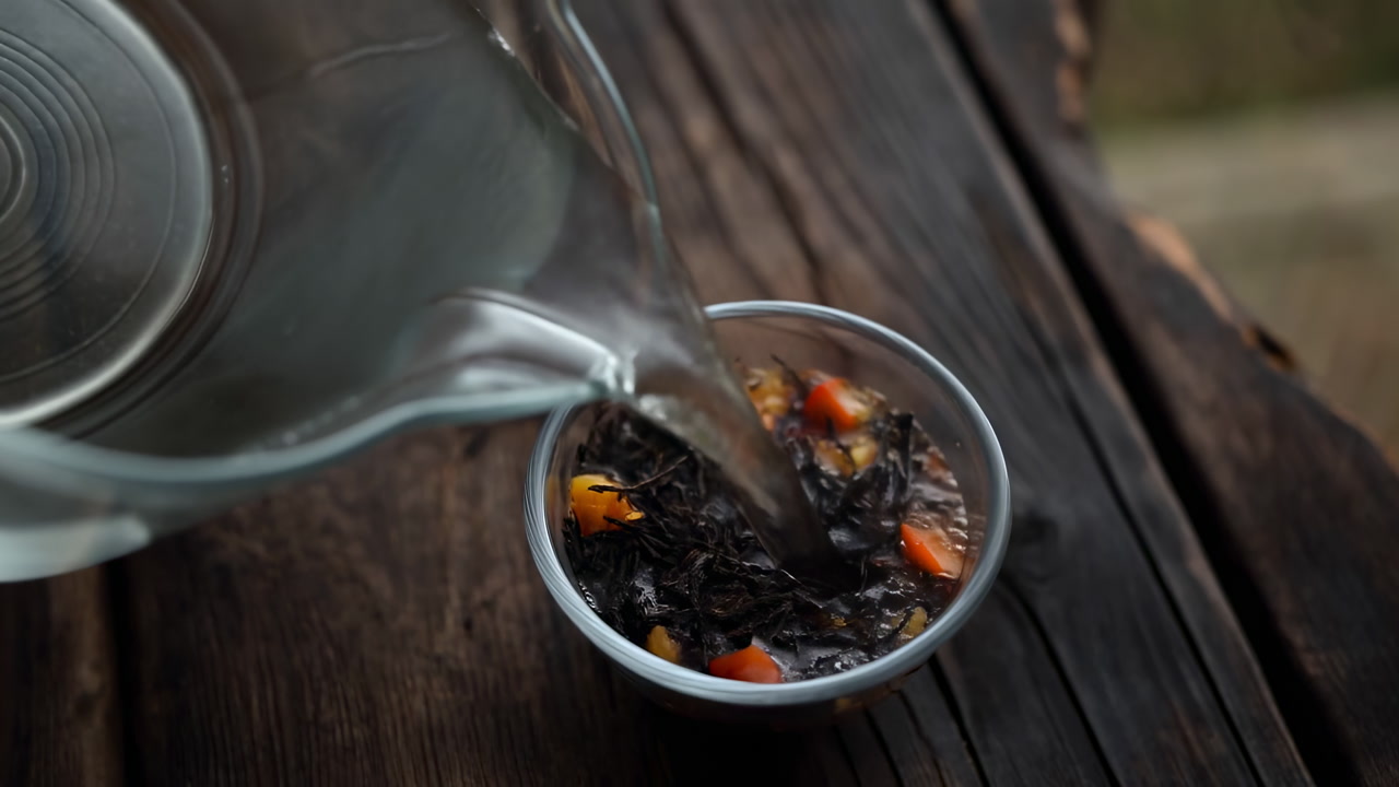 Pouring Glass Pitcher Over Loose Tea In Small Bowl On Rustic Wooden Table, Closeup Of Water Cascading Into Mix