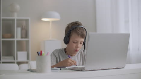 little-boy-is-using-laptop-and-headphones-and-drawing-by-colored-pencils-at-home-happy-childhood