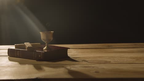 religious concept shot of bible with cross and chalice on wooden table