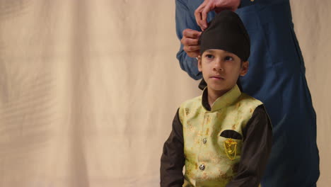 Studio-Shot-Of-Father-Tying-Turban-Onto-Head-Of-Young-Sikh-Son-Wearing-Traditional-Waistcoat-As-Sequence-Part-3-Of-10