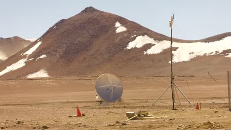 a wide shot of a small telescope at the alma observatory, with the andes mountains behind it