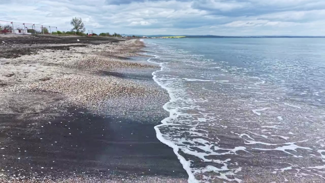 Bølger slår forsiktig mot strandkanten på en strand mens skyer henger på himmelen en kjølig ettermiddag.