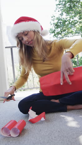vertical video of biracial woman wearing santa hat packing christmas presents, slow motion