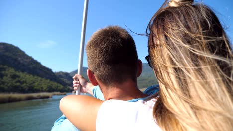 rear back view of young unrecognizable couple spending time together on deck of sailboat at sunny day. beautiful girl hugging her boyfriend from behind on boat during trip. vacation or holiday concept. close up