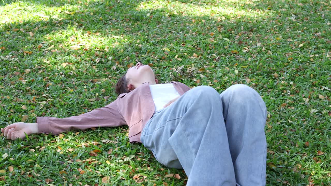 A smiling Thai university student lies on grass, then sits up in bright natural sunlight