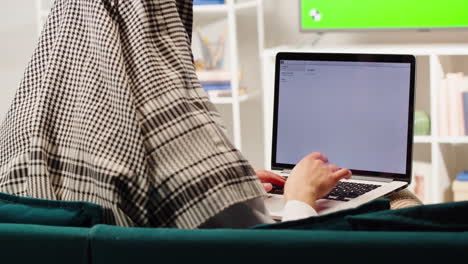 Middle eastern man using laptop close-up, typing on computer keyboard. Television with green screen in living room. Wearing traditional Islamic male clothes