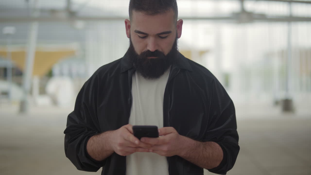 Front view of young bearded man typing message on phone.