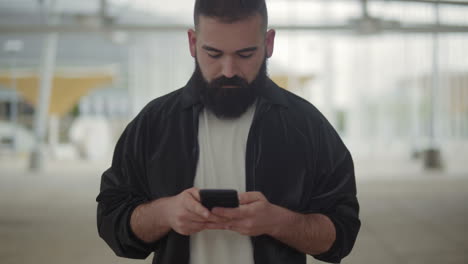 Front-view-of-young-bearded-man-typing-message-on-phone.