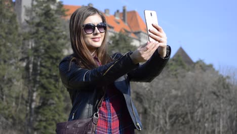 Bastante-Joven-Morena-Con-Gafas-De-Sol-Tomando-Selfies-Con-Un-Castillo-En-Un-Parque-Público