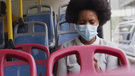 african american businesswoman with face mask using smartphone and sitting in bus