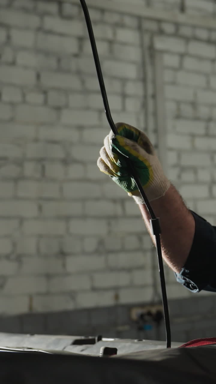 mecánico en uniforme azul utiliza hábilmente una cuña para mantener abierto el capó de un coche negro en un taller mecánico bien iluminado, centrándose en la precisión y la seguridad