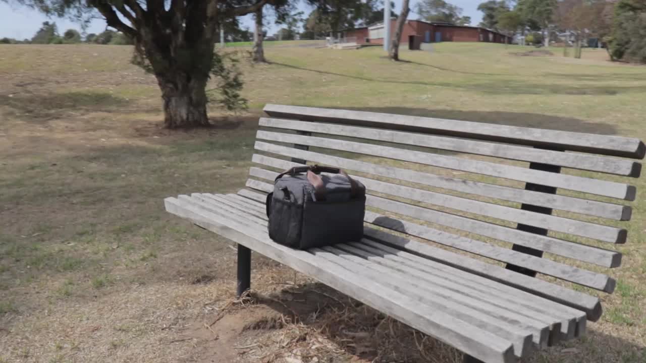나무 공원 벤치 한가운데에 남겨진 작은 회색 파란색 카메라 가방
