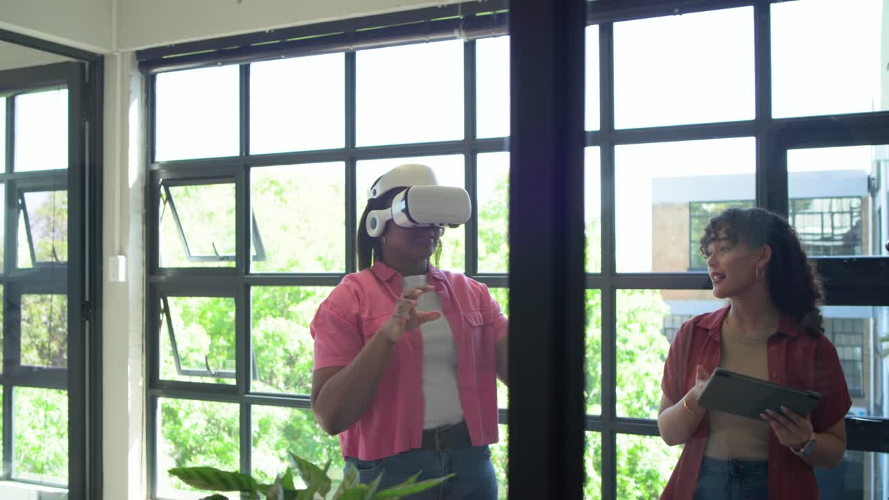 Squadra femminile afroamericana vicino alla finestra, utente VR che fa gesti di pizzicamento e ampi dopo un segnale dal tablet.