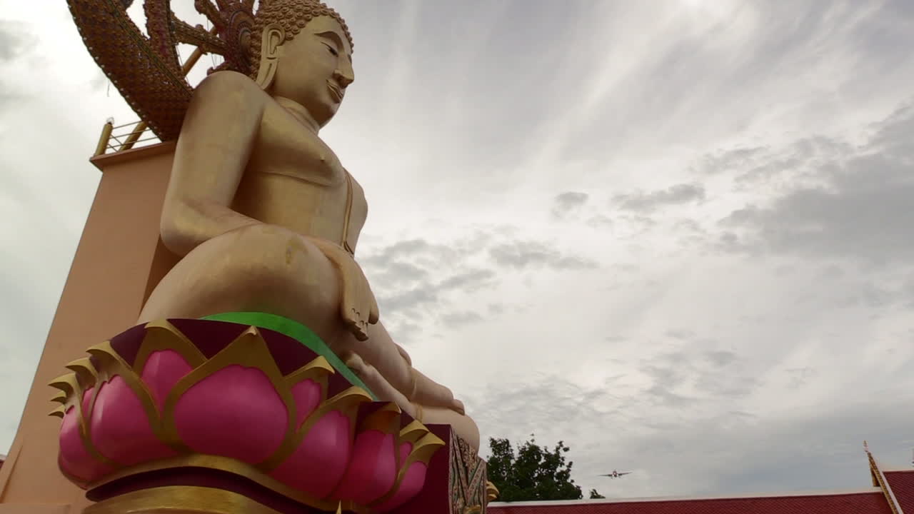 departing airplane flying low over a Buddha statue on a cloudy day