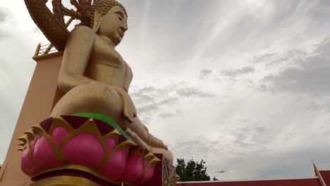 departing airplane flying low over a buddha statue on a cloudy day