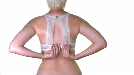 a woman unclasping her white lacy bra on a white seamless studio background