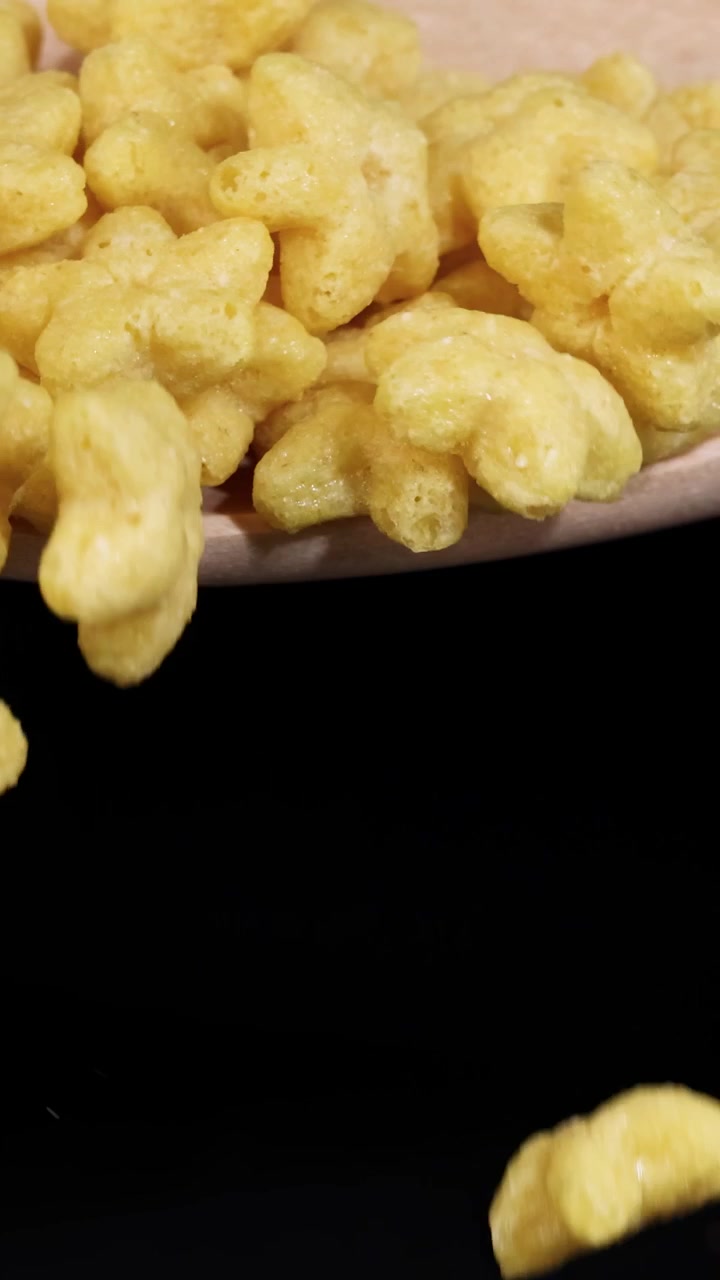 Pezzi di cereali a forma di stella cadono da un cucchiaio su uno sfondo nero, ripresi al rallentatore.