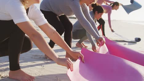 multi-ethnic group of women setting up sport mats on the beach and blue sky background