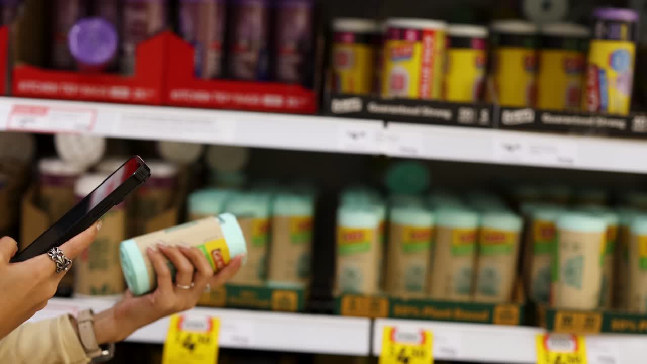 A person uses a smartphone while selecting products in a well-lit supermarket aisle