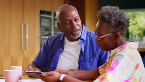 Senior-Couple-Sitting-Around-Table-At-Home-Reviewing-Finances-Using-Digital-Tablet