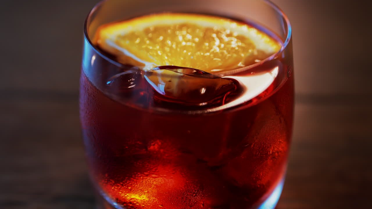 Primo piano di un cocktail Negroni con fetta d'arancia e cubetti di ghiaccio su un tavolo di legno