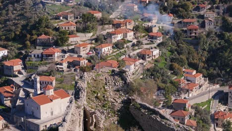 Quaint-village-of-Karytaina-sits-below-castle-wall-and-flagpole,-aerial-dolly-reveal