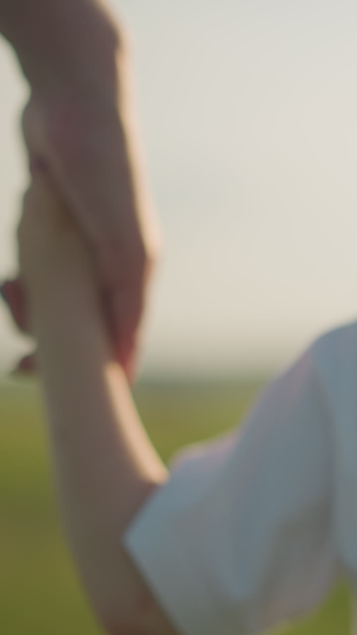 색 셔츠를 입은 어린 소년이 파란색 드레스를 입은 여자와 손을 잡고, 그녀의 얼굴이 보이지 않고, 빛이 빛나는, 흐릿한 풀을 걸어가는 뒷면의 클로즈업